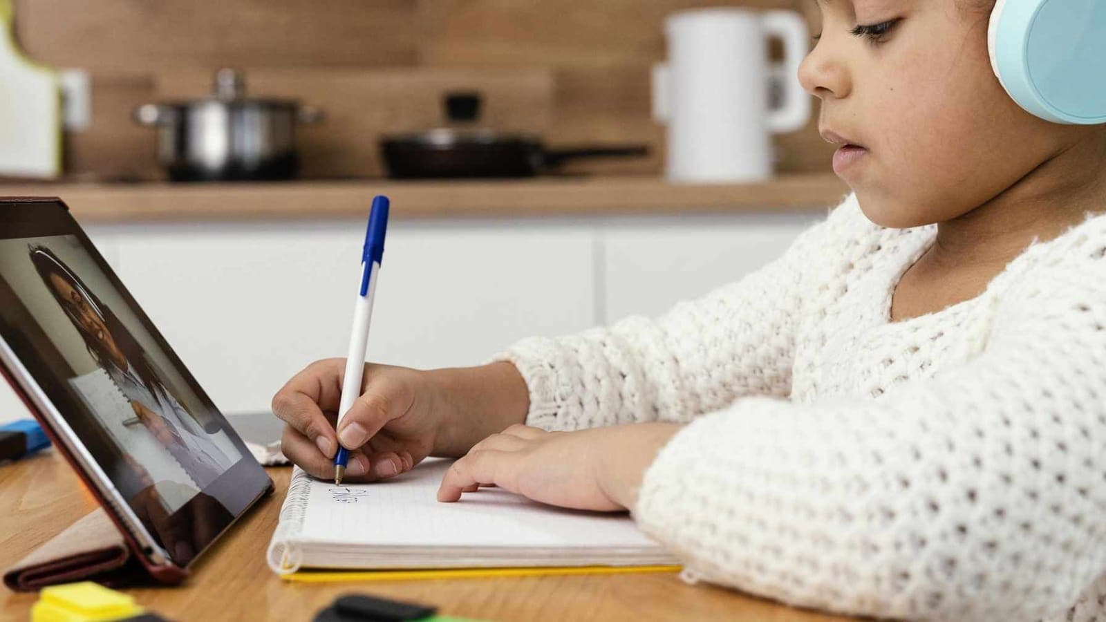 Tifel b'headphones jikteb f'kopja waqt li jsegwi lezzjoni bil-vidjo fuq tablet